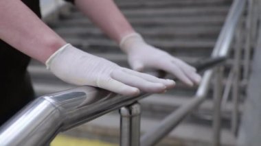 Tıbbi lastik eldivenli bir adamın elleri tırabzanlara değiyor.