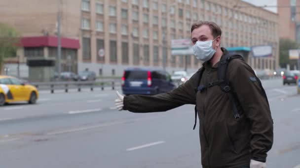 Man i en medicinsk mask och medicinska gummihandskar försöker fånga en taxi på en upptagen motorväg — Stockvideo