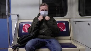 Tıbbi maskeli adam metro kabinine girer boş koltuğa oturur ve telefonda bir mesaj okur.
