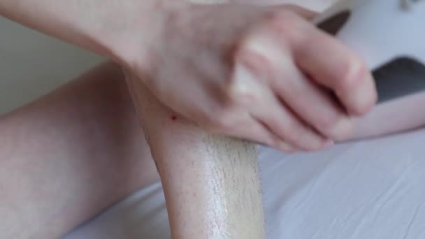 Woman hands apply wax on hairy leg, stick a depilation strip and remove it from skin — Stock Video
