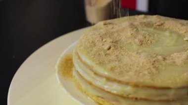 Pasta yuvarlak, dönen ahşap tepside dönüyor ve tepesine bir parça ezilmiş kek serpiştiriyor. 