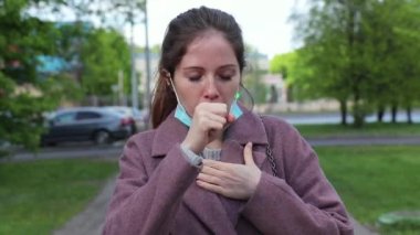 Tıbbi maskeli bir kadın sokakta yürür ve aniden öksürür.