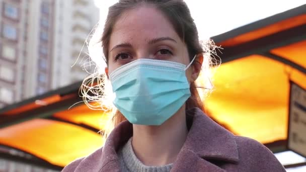 Retrato de una mujer joven con una máscara médica mirando a la cámara sobre un fondo de destello solar — Vídeo de stock