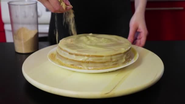 Γυναίκα χέρια πασπαλίζουν κέικ με συνθλιβεί κέικ και στρίψτε το σε ένα στρογγυλό ξύλινο περιστρεφόμενο δίσκο — Αρχείο Βίντεο