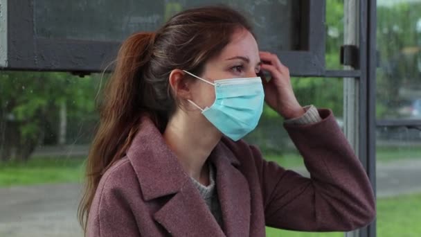 Vrouw met een medisch masker wacht op een bus en hoest slecht — Stockvideo