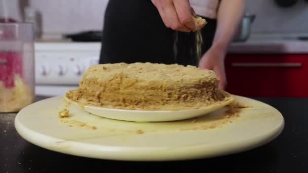 Woman hands sprinkle cake with crushed cakes on a wooden spinning tray — Stock Video