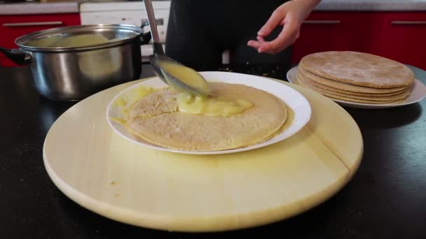 Vrouw smeert crème op de top van een taart die op een ronde houten spinning lade — Stockvideo