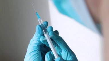 Tıbbi maskeli doktor elinde bir şırınga tutuyor ve iğne yapmaya hazırlanıyor.