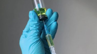 Ellerinde plastik eldiven, şırıngayı tutuyor ve ilacı ampulden alıyor.