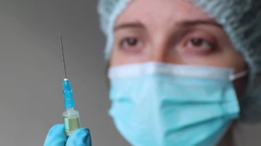Doktor elinde bir şırınga tutuyor ve yüzüne bakıyor. 