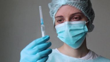 Tıbbi maskeli doktor şırıngaya bakar, kapağını çıkarır ve iğneyi yapmaya hazırlanır.