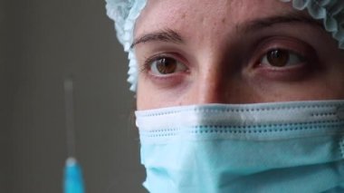 Doktor elinde bir şırınga tutuyor ve arka plandaki iğneye bakıyor.