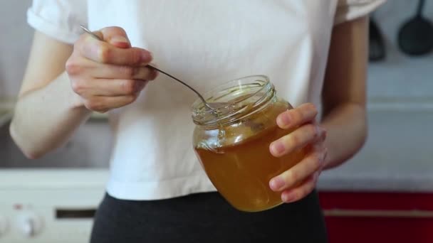 Mujer toma miel con una cuchara de un frasco y lo añade al plato — Vídeo de stock