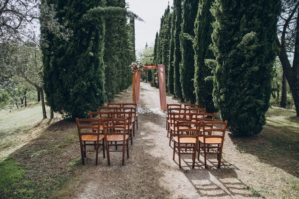 結婚式だ トスカーナのヒノキ通りには 花の組成とピンクの布で飾られた結婚式のためのアーチがあり 近くにはゲストのための椅子があります — ストック写真