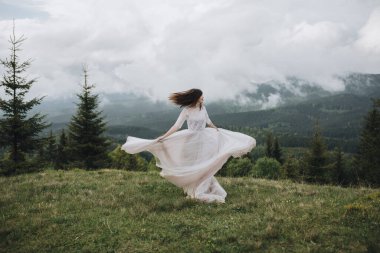 Dağlarda bahar düğünü. Beyaz elbiseli genç bir kız dağlarda yeşil bir çayırda koşuyor.