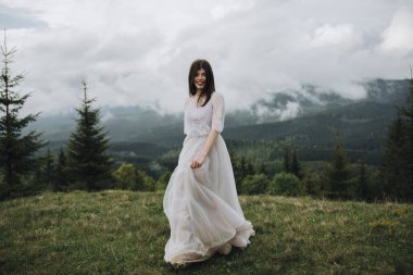 Dağlarda bahar düğünü. Beyaz elbiseli genç bir kız dağlarda yeşil bir çayırda koşuyor.