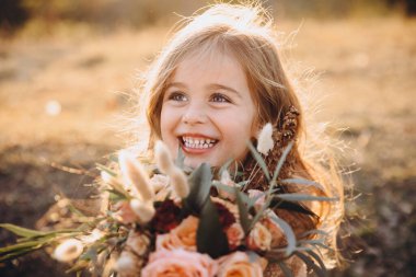 Gün batımında sonbahar dağlarında elinde bir buket çiçekle dikilen şık, güzel bir kızın portresi.