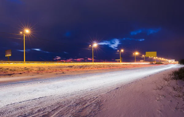 Winter snowy highway at night shined with lamps