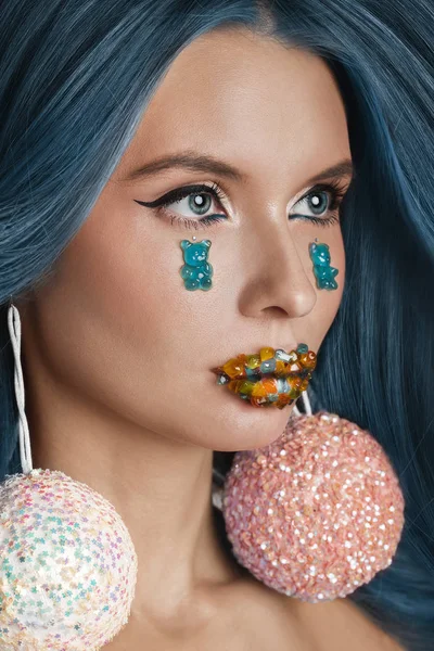 Art beauty portrait of a model with blue fluttering hair and unusual make-up with jelly bears on cheeks and color jelly on a lips. Art beauty concept.