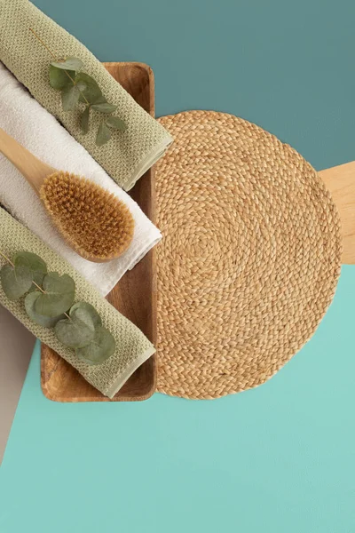 Bathroom spa set with body brush and towels on straw napkin decorated eucalyptus leaves. Geometric background. Body care concept.
