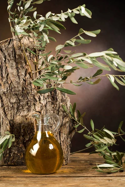 Panenský olivový olej skleněná nádoba a listí na pozadí kmen olivovníku — Stock fotografie