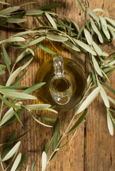 Panenský olivový olej skleněná nádoba a listí na dřevěný stůl. — Stock fotografie
