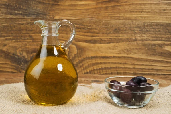 Panenský olivový olej skleněná nádoba a čerstvými olivami na pytlovina a dřevěné — Stock fotografie