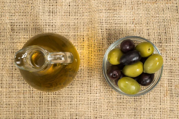 Panenský olivový olej skleněná nádoba a čerstvými olivami na pytlovina. — Stock fotografie