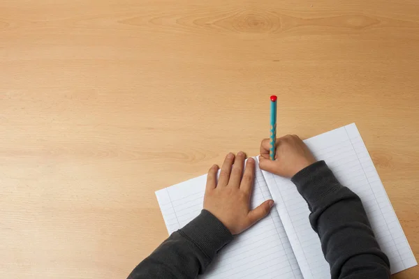 Çocuk bir defter üzerinde yazıyor.