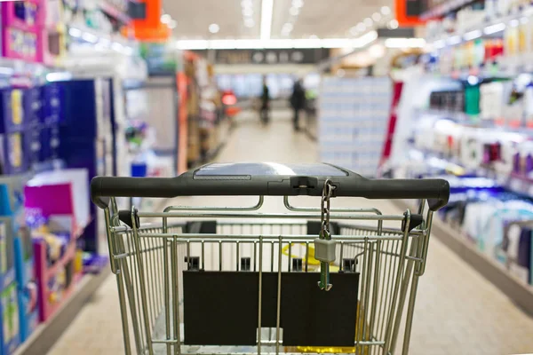 Carrinho de compras cheio de supermercado no corredor do supermercado borrado . — Fotografia de Stock