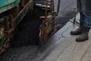 Workers using asphalt tools during road construction.