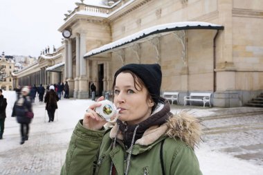 Genç kadın, Karlovy Vary'da doğal bir kaplıca tedavi maden suyu fincanla içme kış aylarında, Çek Cumhuriyeti