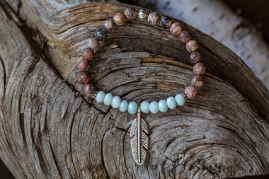 Tahta zemin üzerinde metal tüy kolyesi olan mineral taşı yoga bilekliği.