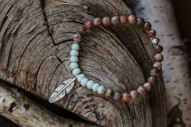 Tahta zemin üzerinde metal tüy kolyesi olan mineral taşı yoga bilekliği.