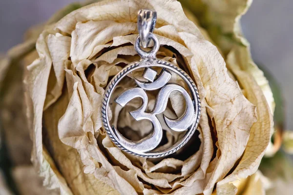 Sterling silver pendant in shape of om symbol in cyrcle placed on dried rose