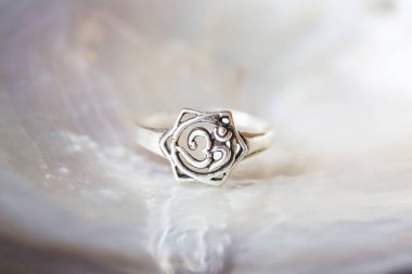 Gümüş yüzük, beyaz inci arkaplanlı, om şeklinde küçük mücevher parçası.