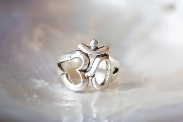 Silver ring tiny jewelry piece on white pearl background in the shape of om