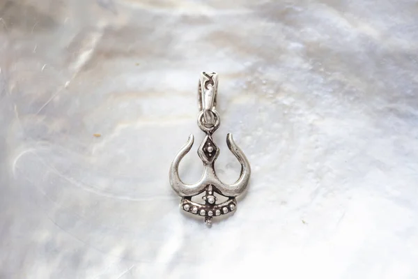 sterling silver metal pendant on natural background in the shape of the shiva symbol