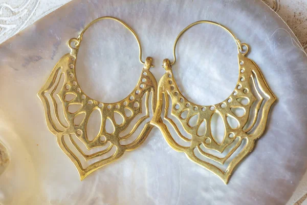 白色外壳自然背景上的东方荷花形状的黄铜金属耳环 — 图库照片