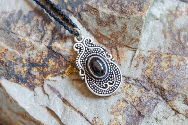 Kayalık arka planda doğal obsidiyen değerli taşlı pirinç kolye.