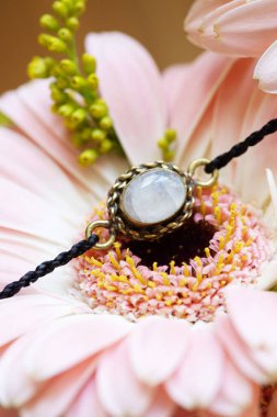 Pembe çiçekte ay taşı bileziği olan küçük metal bir kolye parçası. 