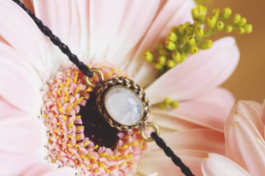 Pembe çiçekte ay taşı bileziği olan küçük metal bir kolye parçası. 