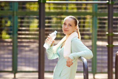Spor salonundaki kadın spor yaptıktan sonra dinleniyor, dinleniyor, açık hava spor salonundan temiz su içiyor.