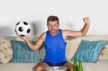 genç çekici adam mutlu ve heyecanlı izlerken futbol maçı televizyonda zafer hedef deli ve spastik bira patlamış mısır ve futbol topu ile kutluyor 