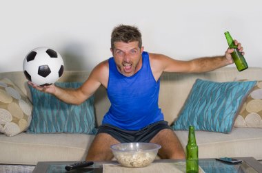 genç çekici adam mutlu ve heyecanlı izlerken futbol maçı televizyonda zafer hedef deli ve spastik bira patlamış mısır ve futbol topu ile kutluyor 