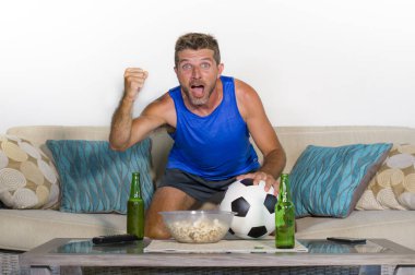 genç çekici adam mutlu ve heyecanlı izlerken futbol maçı televizyonda zafer hedef deli ve spastik bira patlamış mısır ve futbol topu ile kutluyor 