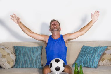 genç çekici adam mutlu ve heyecanlı izlerken futbol maçı televizyonda zafer hedef deli ve spastik bira patlamış mısır ve futbol topu ile kutluyor 