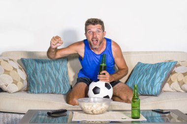 genç çekici adam mutlu ve heyecanlı izlerken futbol maçı televizyonda zafer hedef deli ve spastik bira patlamış mısır ve futbol topu ile kutluyor 