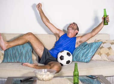 genç çekici adam mutlu ve heyecanlı izlerken futbol maçı televizyonda zafer hedef deli ve spastik bira patlamış mısır ve futbol topu ile kutluyor 