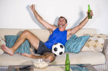 genç çekici adam mutlu ve heyecanlı izlerken futbol maçı televizyonda zafer hedef deli ve spastik bira patlamış mısır ve futbol topu ile kutluyor 